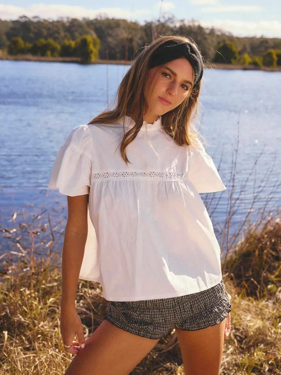 Woman in a white eyelet blouse and gingham shorts by a lake