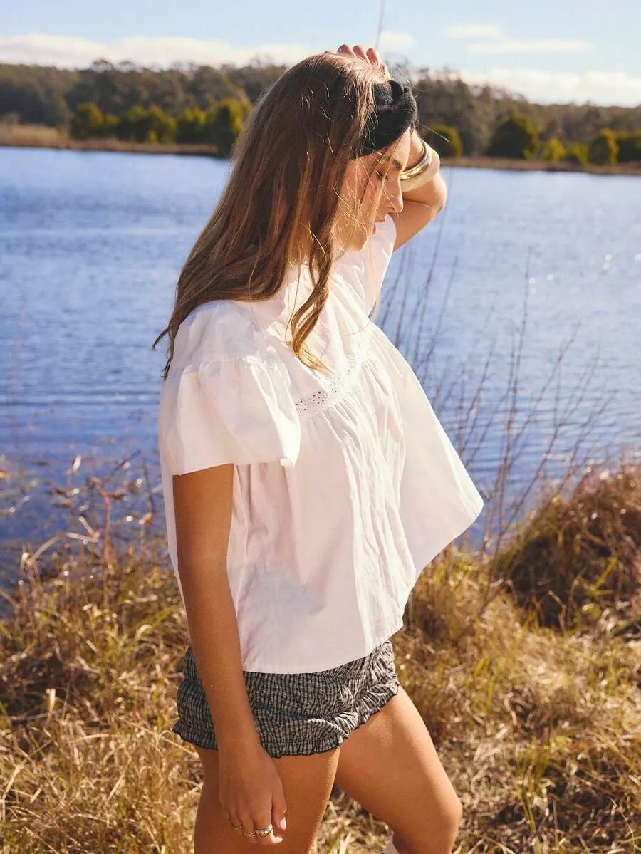 Woman in a white flutter-sleeve blouse walking by a lake